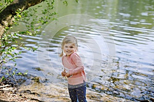 Cute little toddler girl feeding wild geese family in a forest park. Happy child having fun with observing birds and