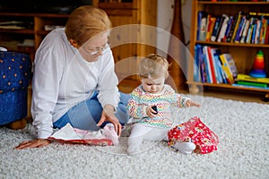 Cute little toddler girl and grandmother playing with toys at home. Adorable baby child and senior retired woman