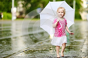 Cute little toddler girl having fun under a rain