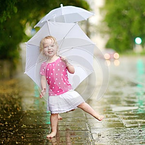 Cute little toddler girl having fun under a rain