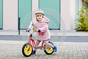 Cute little toddler girl with helmet riding on run balance bike to daycare, playschool or kindergarden. Happy child