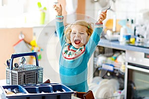 Cute little toddler girl helping in the kitchen with dish washing machine. Happy healthy blonde child sorting knives