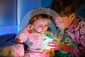 Cute little toddler girl and kid boy playing with colorful night light lamp before going to bed. Sleepy tired baby