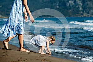 Cute little toddler girl and mother in blue dresses runnig and playing with waves on the wild beach. Turkey, Iztuzu beach,  Dalyan