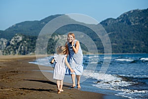 Cute little toddler girl and mother in blue dresses runnig and playing with waves on the wild beach. Turkey, Iztuzu beach,  Dalyan