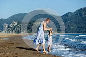 Cute little toddler girl and mother in blue dresses runnig and playing with waves on the wild beach. Turkey, Iztuzu beach,  Dalyan