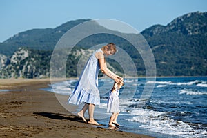 Cute little toddler girl and mother in blue dresses runnig and playing with waves on the wild beach. Turkey, Iztuzu beach,  Dalyan