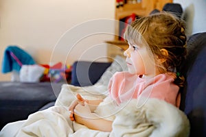 Cute little toddler girl in nightwear pajamas watching cartoons or movie on tv. Happy healthy baby child at home.