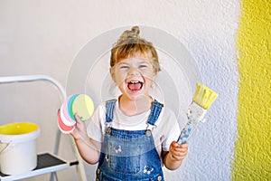 Cute little toddler girl painting the wall with yellow color in new house. Family repair apartment home. Happy child