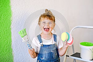 Cute little toddler girl painting the wall with yellow color in new house. Family repair apartment home. Happy child