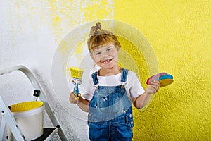 Cute little toddler girl painting the wall with yellow color in new house. Family repair apartment home. Happy child