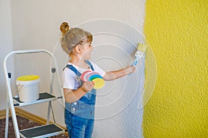 Cute little toddler girl painting the wall with yellow color in new house. Family repair apartment home. Happy child