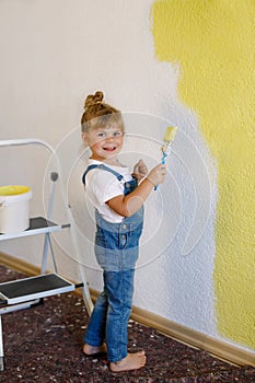 Cute little toddler girl painting the wall with yellow color in new house. Family repair apartment home. Happy child