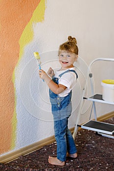 Cute little toddler girl painting the wall with yellow color in new house. Family repair apartment home. Happy child