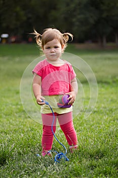 Cute Little toddler girl in pink dress playing in park in front of green grass