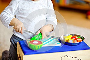 Cute little toddler girl playing at home with eco wooden toys. Happy healthy excited child cutting vegetables and fruits