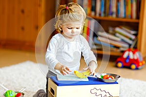 Cute little toddler girl playing at home with eco wooden toys. Happy healthy excited child cutting vegetables and fruits