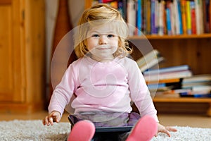 Cute little toddler girl playing with tablet pc at home. Healthy baby touching pad with fingers, looking cartoons and