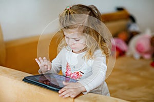 Cute little toddler girl playing with tablet pc at home. Healthy baby touching pad with fingers, looking cartoons and