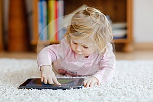 Cute little toddler girl playing with tablet pc at home. Healthy baby touching pad with fingers, looking cartoons and