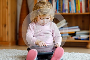 Cute little toddler girl playing with tablet pc at home. Healthy baby touching pad with fingers, looking cartoons and