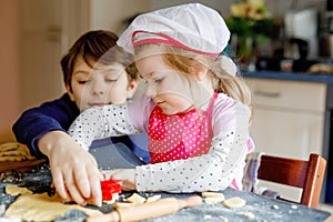 Cute little toddler girl and preteen kid boy baking Easter cookies at home indoors. Children, siblings with apron and