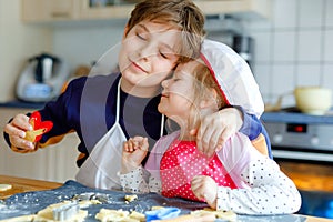 Cute little toddler girl and preteen kid boy baking Easter cookies at home indoors. Children, siblings with apron and