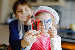 Cute little toddler girl and preteen kid boy baking Easter cookies at home indoors. Children, siblings with apron and