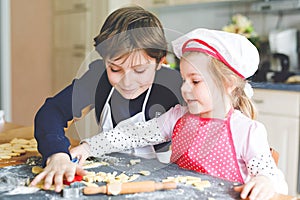 Cute little toddler girl and preteen kid boy baking Easter cookies at home indoors. Children, siblings with apron and chef hat cut