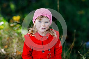 Cute little toddler girl in red coat making a walk through autumn forest. Happy healthy baby enjoying walking with