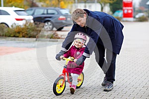 Cute little toddler girl in safety helmet riding on run balance bike. Middle-aged father teaching happy healthy lovely