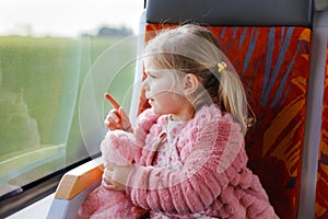 Cute little toddler girl sitting in train and looking out of window while moving. Adorable happy healthy baby child