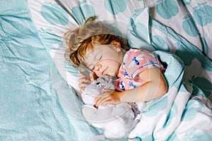 Cute little toddler girl sleeping in bed with favourite soft plush toy dog. Adorable baby child dreaming, healthy sleep