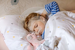 Cute little toddler girl sleeping in bed with favourite soft plush toy lama. Adorable baby child dreaming, healthy sleep