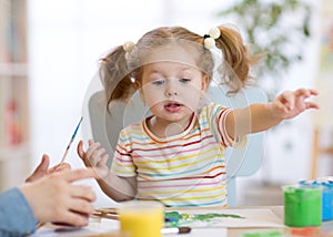 Cute little toddler girl in striped shirt and pony tails paints in the art class