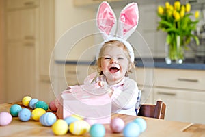 Cute little toddler girl wearing Easter bunny ears playing with colored pastel eggs. Happy baby child unpacking gifts