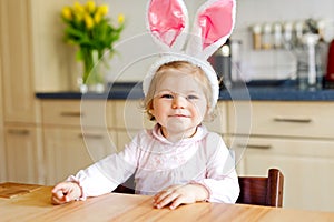 Cute little toddler girl wearing Easter bunny ears playing with colored pastel eggs. Happy baby child unpacking gifts