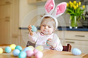 Cute little toddler girl wearing Easter bunny ears playing with colored pastel eggs. Happy baby child unpacking gifts