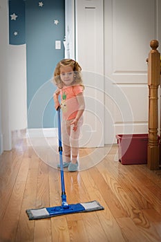 Cute little white girl is helping to clean the house. She holds a mop