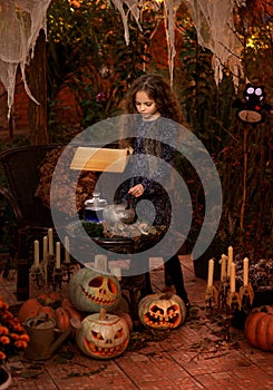 Cute little witch cooking a potion in the decorated garden.