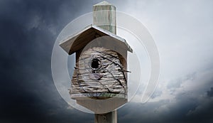 Cute wooden birdhouse with straw walls on a wooden post