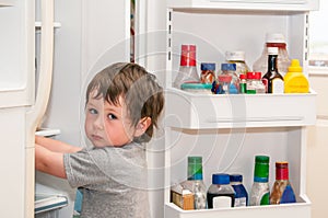 Cute llittle boy getting something to eat out of the refridgerator