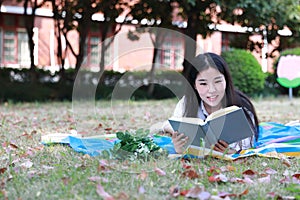 Cute lovely Asian Chinese pretty girl wear student suit in school lying on grass lawn reading book enjoy causian time