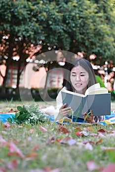 Cute lovely Asian Chinese pretty girl wear student suit in school lying on grass lawn reading book enjoy causian time