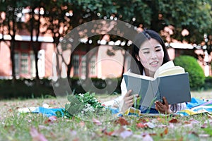 Cute lovely Asian Chinese pretty girl wear student suit in school lying on grass lawn reading book enjoy causian time