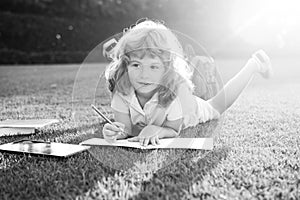 Cute lovely child with pencil writing on notebook outside. Kid read book in park.