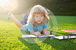 Cute lovely child with pencil writing on notebook outside. Kid read book in park.