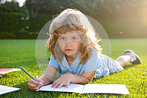 Cute lovely child with pencil writing on notebook outside. Kid read book in park. Summer vacation homework. Preschool