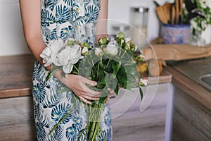 Cute and lovely peony flowers in women`s hands.. many layered petals. Bunch pale white peonies flowers light gray background