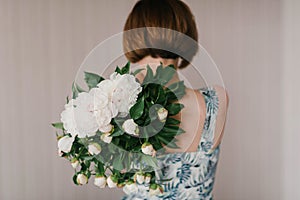 Cute and lovely peony flowers in women`s hands.. many layered petals. Bunch pale white peonies flowers light gray background